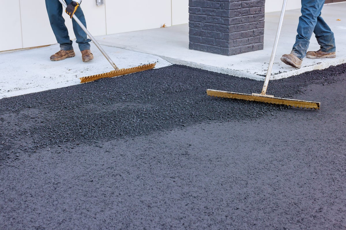 Workers spreading freshly laid tarmac on a residential driveway with rakes