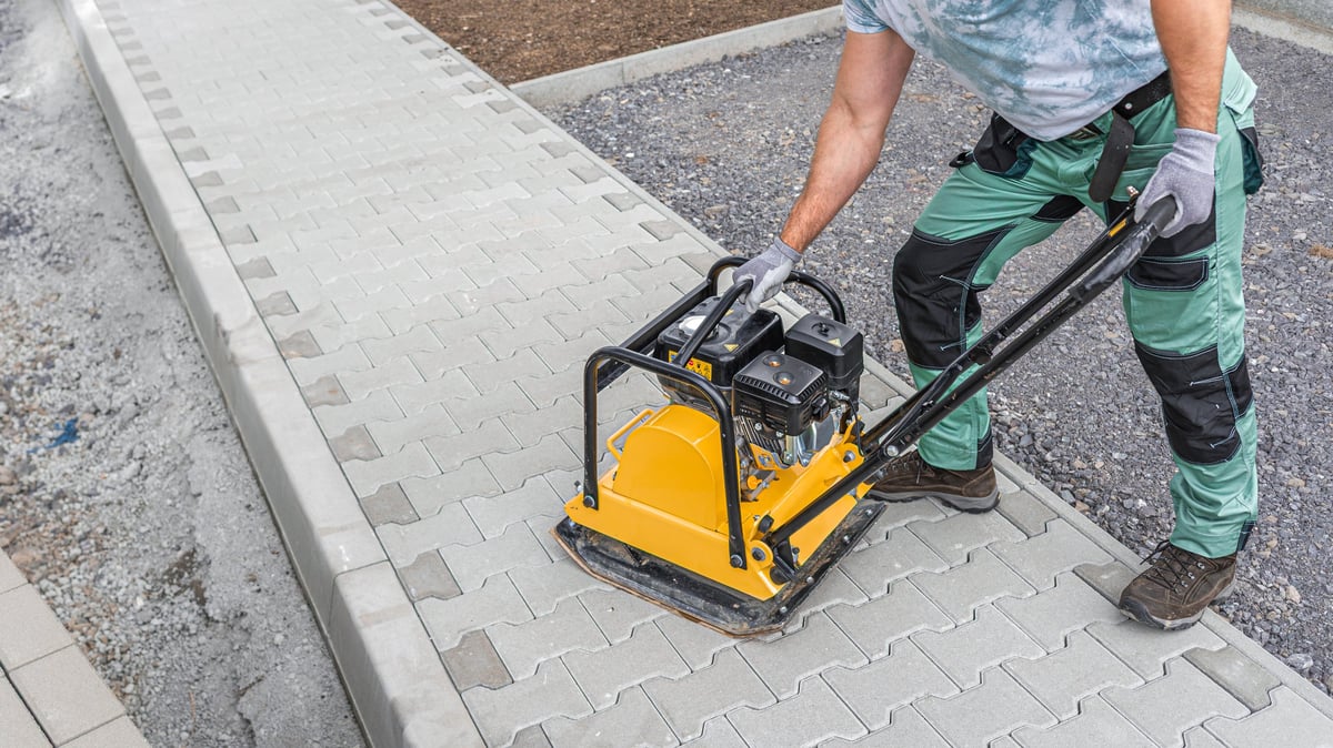 Worker compacting block paving with vibration plate during driveway installation